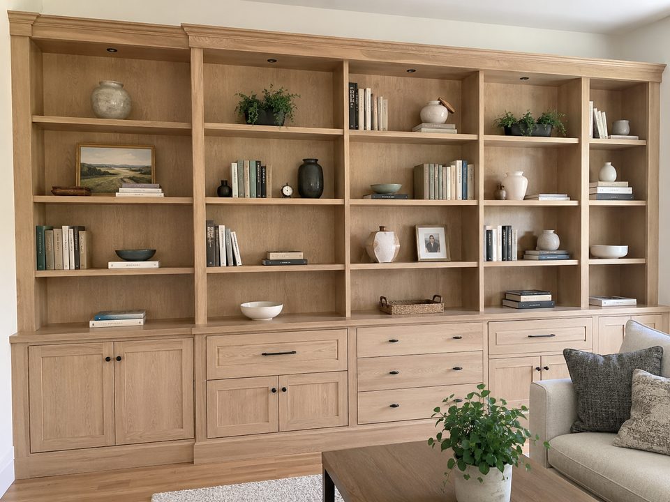 Floor-to-ceiling white oak bookshelf wall with base cabinets and adjustable shelving